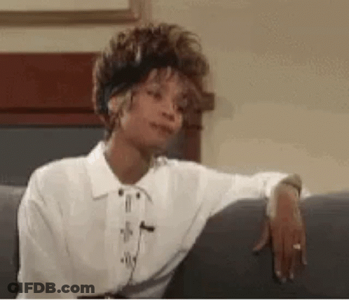 A Woman In A White Shirt Is Sitting On A Couch With Her Hand On Her Elbow . GIF