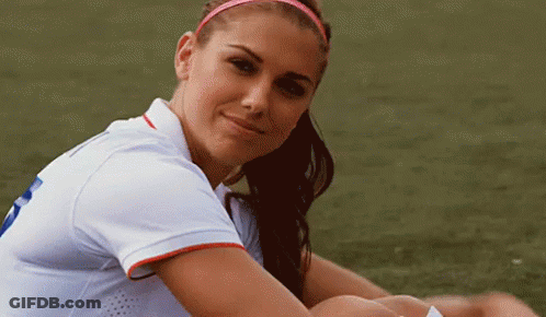 A Woman In A White Shirt Is Sitting On A Soccer Field . GIF
