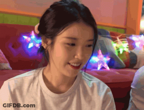 A Woman In A White Shirt Is Smiling In Front Of A Colorful Couch GIF