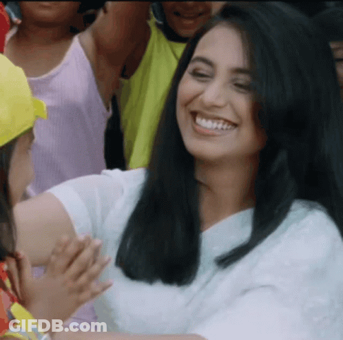A Woman In A White Shirt Is Smiling In Front Of A Crowd Of People GIF