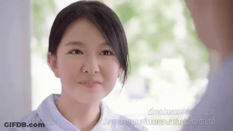 A Woman In A White Shirt Is Smiling In Front Of A Sign That Says 265/2561 GIF