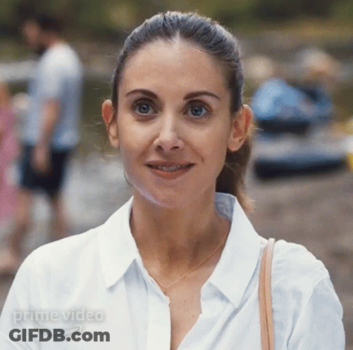 A Woman In A White Shirt Is Smiling In Front Of A Sign That Says Prime Video On It GIF