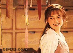 A Woman In A White Shirt Is Smiling In Front Of A Wall With Ribbons Hanging From It . GIF