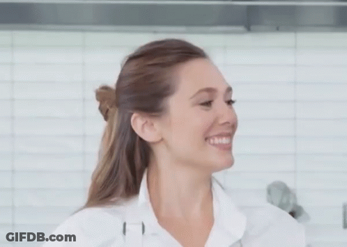 A Woman In A White Shirt Is Smiling In Front Of A White Tiled Wall . GIF