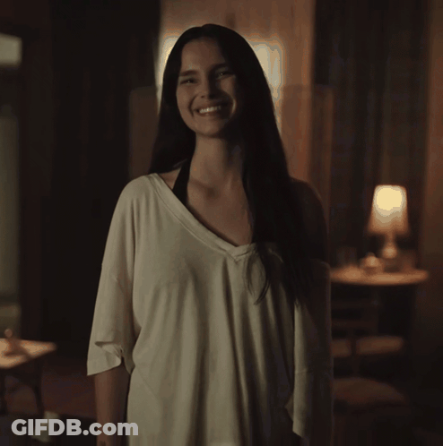 A Woman In A White Shirt Is Smiling In The Dark GIF