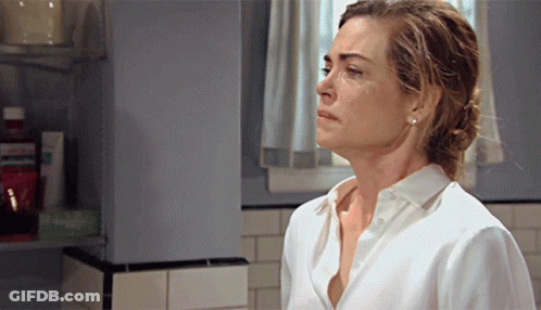 A Woman In A White Shirt Is Standing In A Bathroom Looking Down GIF