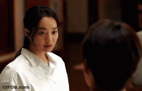 A Woman In A White Shirt Is Standing Next To A Man And Looking At Him . GIF