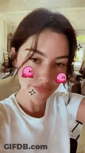 A Woman In A White Shirt Is Taking A Selfie With A Kirby Filter On Her Face . GIF
