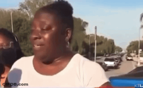 A Woman In A White Shirt Is Talking Into A Microphone While Standing On A City Street . GIF