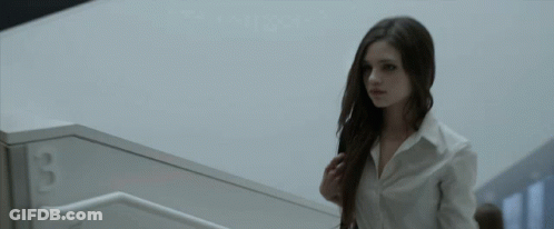 A Woman In A White Shirt Is Walking Down A Set Of Stairs With The Number 3 On The Wall Behind Her GIF