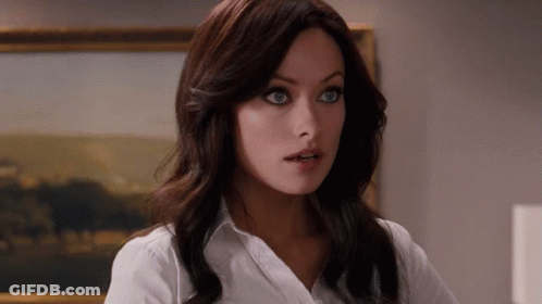 A Woman In A White Shirt Stands In Front Of A Framed Painting GIF