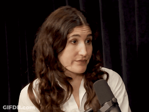 A Woman In A White Shirt Stands In Front Of A Microphone Making A Funny Face GIF