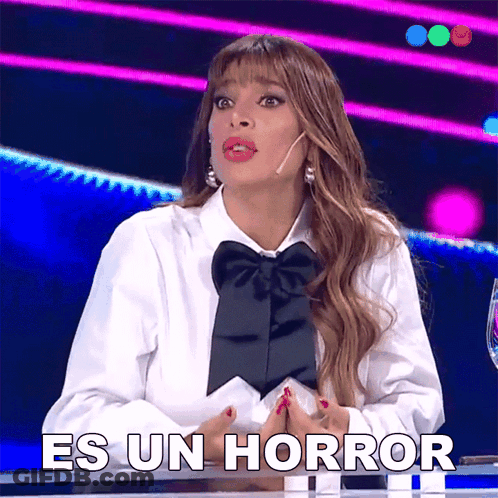 A Woman In A White Shirt With A Black Bow Tie Is Sitting At A Table Saying Es Un Horror GIF