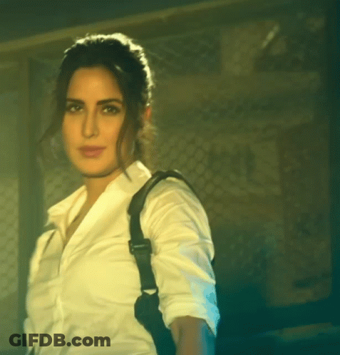 A Woman In A White Shirt With A Black Strap On Her Back GIF