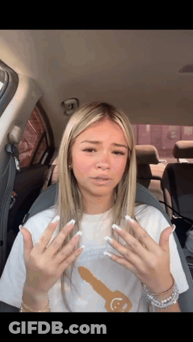 A Woman In A White Shirt With A Key On It Is Sitting In The Back Seat Of A Car GIF