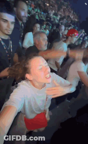 A Woman In A White Shirt With A Red Purse Is Dancing In A Crowd GIF