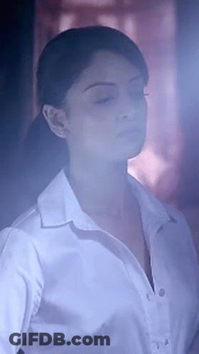 A Woman In A White Shirt With Her Eyes Closed Is Standing In A Dark Room . GIF