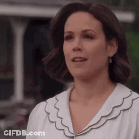 A Woman In A White Shirt With Ruffles On The Collar Is Looking At The Camera . GIF