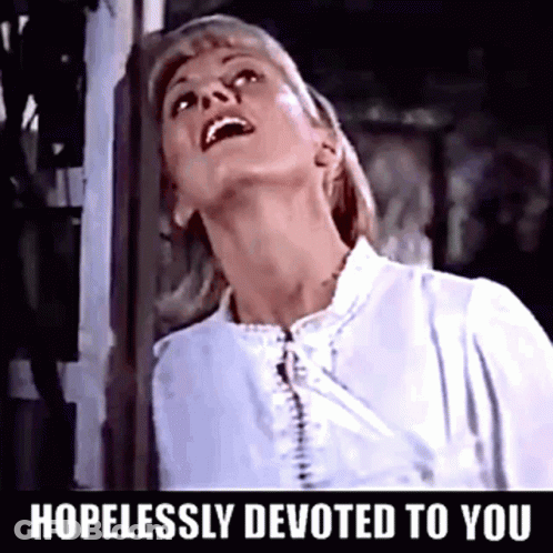 A Woman In A White Shirt With The Words Hopelessly Devoted To You Below Her GIF
