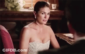 A Woman In A White Strapless Dress Is Sitting At A Table With A Man . GIF