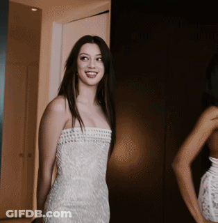 A Woman In A White Strapless Dress Is Smiling In Front Of A Mirror GIF