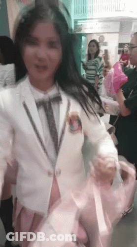 A Woman In A White Suit And Tie Is Holding A Pink Balloon GIF