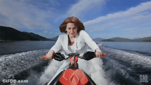 A Woman In A White Suit Is Riding A Jet Ski With The Nbc Logo Behind Her GIF