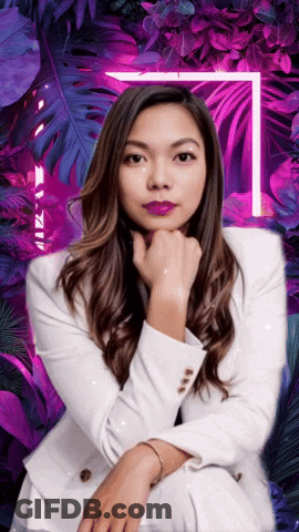 A Woman In A White Suit Is Sitting In Front Of Purple Leaves GIF