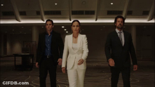A Woman In A White Suit Is Standing In Between Two Men In Suits GIF