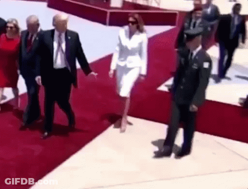 A Woman In A White Suit Is Walking On A Red Carpet With A Man In A Suit And Tie . GIF