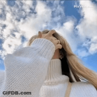 A Woman In A White Sweater Covering Her Face Against A Blue Sky GIF