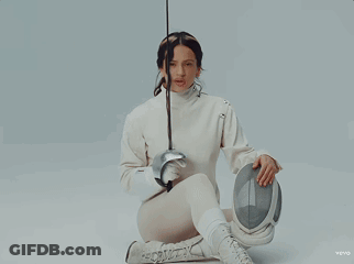 A Woman In A White Sweater Is Holding A Fencing Sword GIF