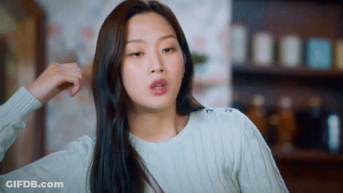 A Woman In A White Sweater Is Holding Her Hair And Making A Funny Face GIF
