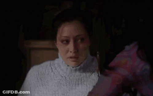 A Woman In A White Sweater Is Looking At Another Woman In A Purple Shirt In A Dark Room . GIF