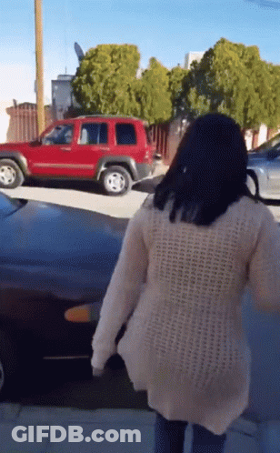 A Woman In A White Sweater Is Walking Down A Street In Front Of A Red Suv GIF