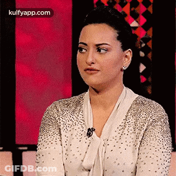 A Woman In A White Sweater With Rhinestones Is Sitting In Front Of A Pink Background . GIF