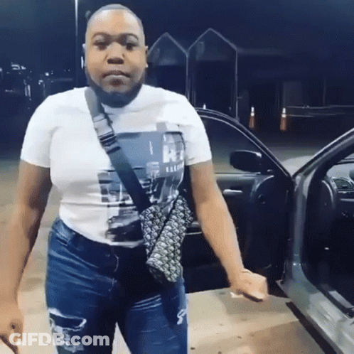 A Woman In A White T-Shirt And Jeans Is Standing In Front Of A Car . GIF