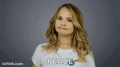 A Woman In A White T-Shirt Is Giving A Peace Sign . GIF