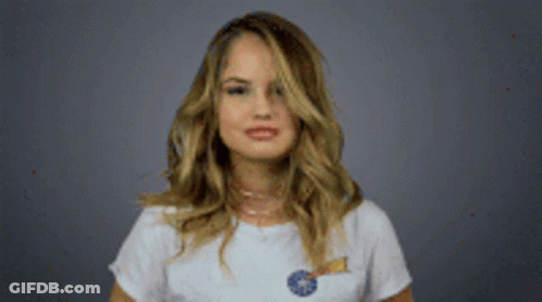 A Woman In A White T-Shirt Is Holding A Lollipop And Making A Funny Face . GIF