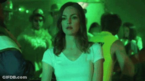 A Woman In A White T-Shirt Is Sitting In A Crowded Room . GIF