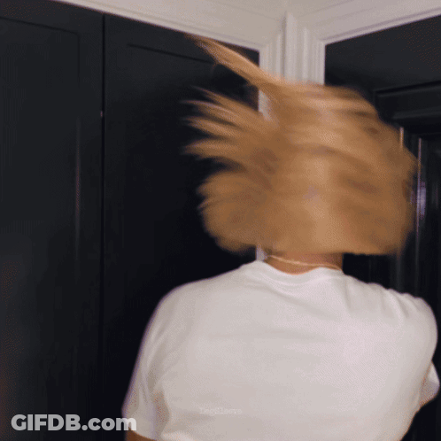 A Woman In A White T-Shirt Is Standing In Front Of A Door GIF