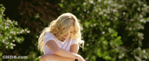 A Woman In A White T-Shirt Is Standing In Front Of Trees GIF
