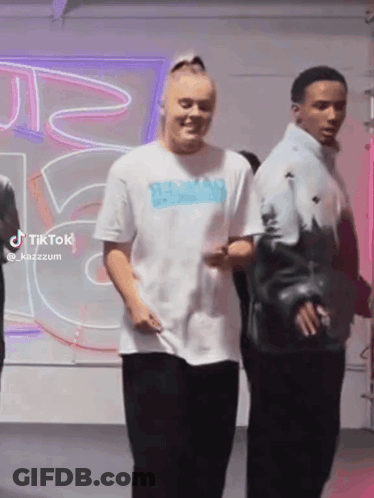 A Woman In A White T-Shirt Is Standing Next To A Man In A Blue Jacket . GIF