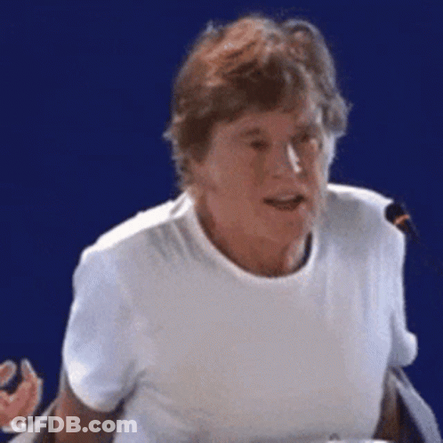 A Woman In A White T-Shirt Is Talking Into A Microphone GIF