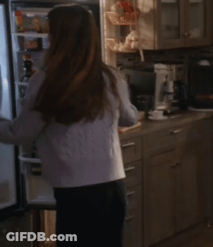 A Woman In A White Tank Top And A Blue Cardigan Is Dancing In The Kitchen GIF
