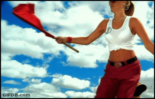 A Woman In A White Tank Top And Red Pants Holds A Red Flag GIF