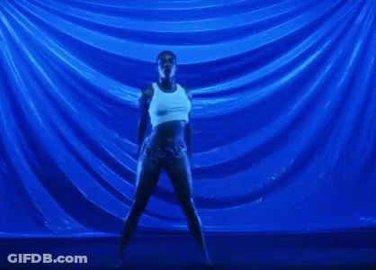 A Woman In A White Tank Top And Shorts Is Dancing In Front Of A Blue Background . GIF