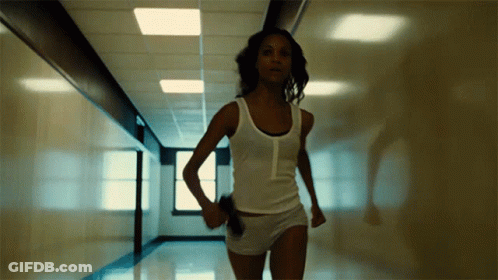 A Woman In A White Tank Top And Shorts Is Running In A Hallway GIF