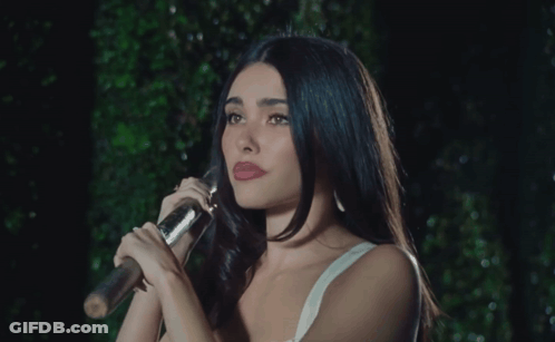 A Woman In A White Tank Top Holds A Microphone GIF
