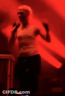 A Woman In A White Tank Top Is Dancing In A Dark Room GIF